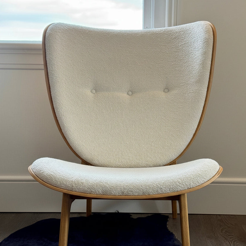 Modern chair with beige cushioned seat and backrest in a room with a window and dark rug.