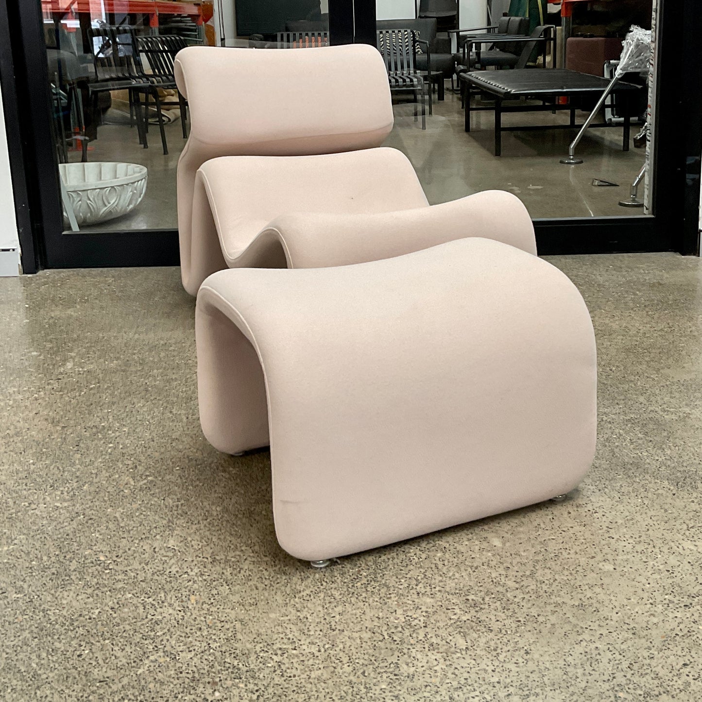 Beige lounge chair and ottoman on a concrete floor with a store interior in the background