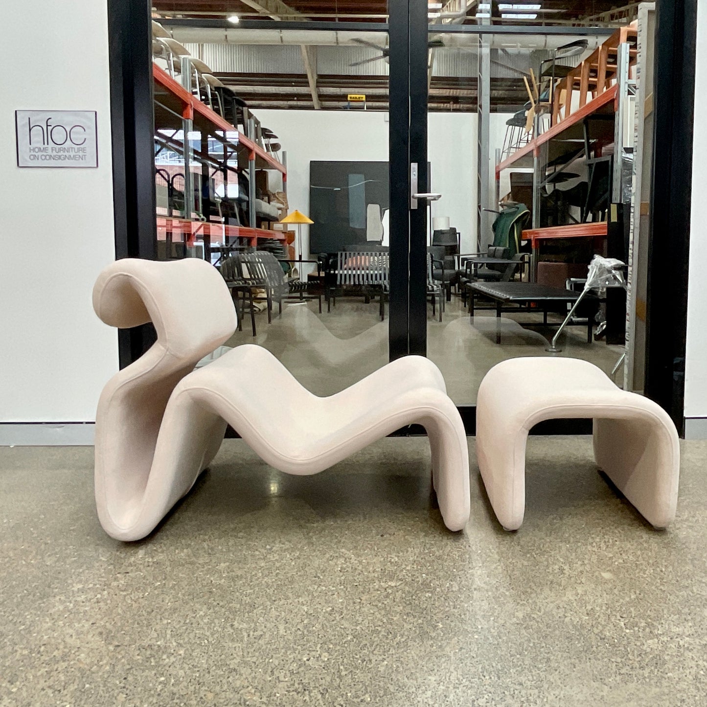 Modern white chair and ottoman in a warehouse setting with glass walls.