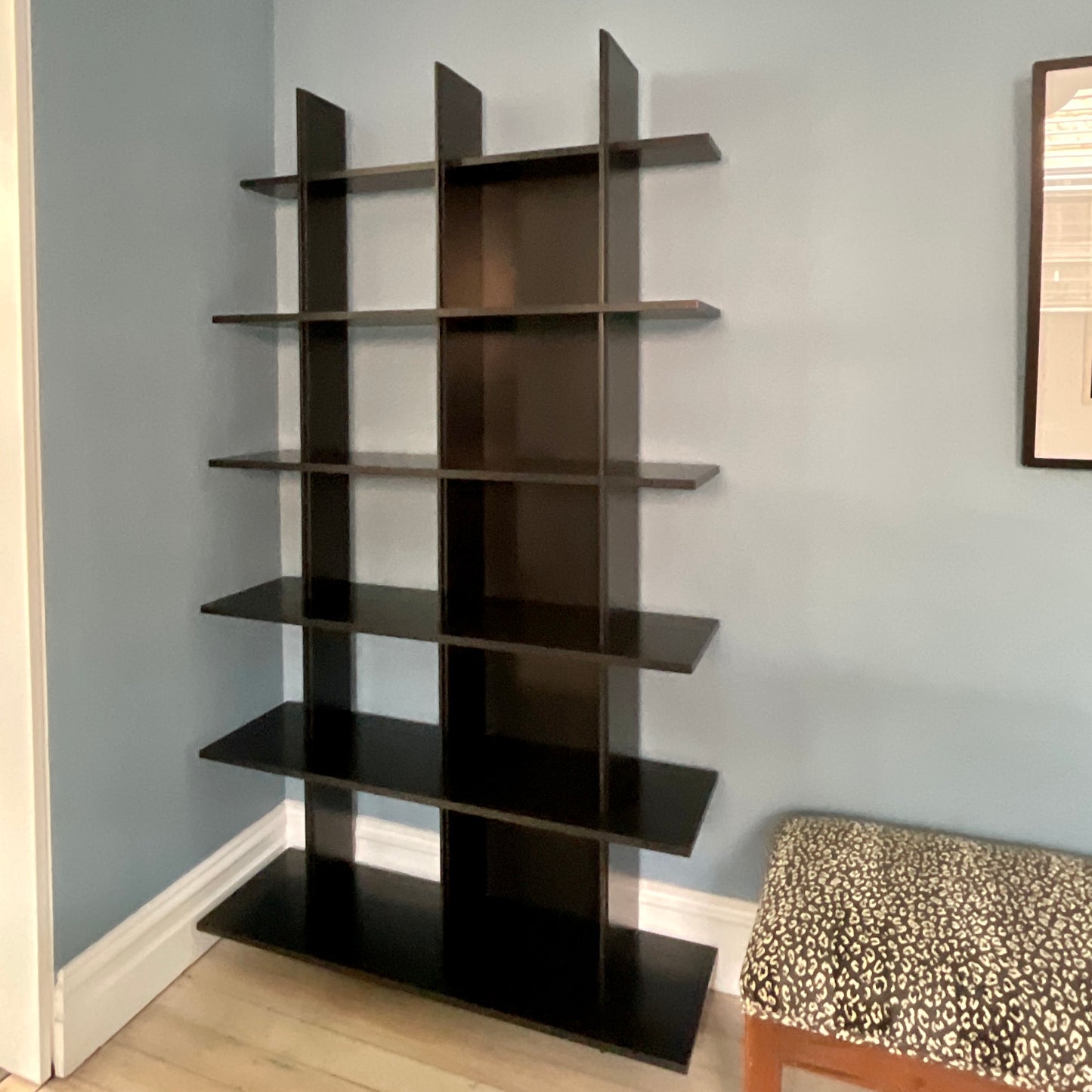 Black shelving unit against a light blue wall with a patterned chair in the foreground.