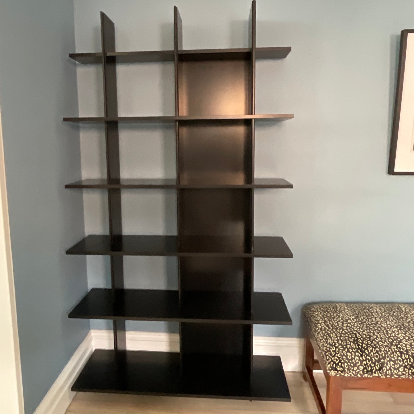Black wall shelf against a light blue wall with a patterned stool in the corner.