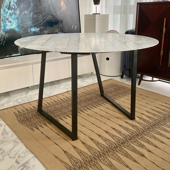 Round marble table with black metal legs in a modern interior setting.