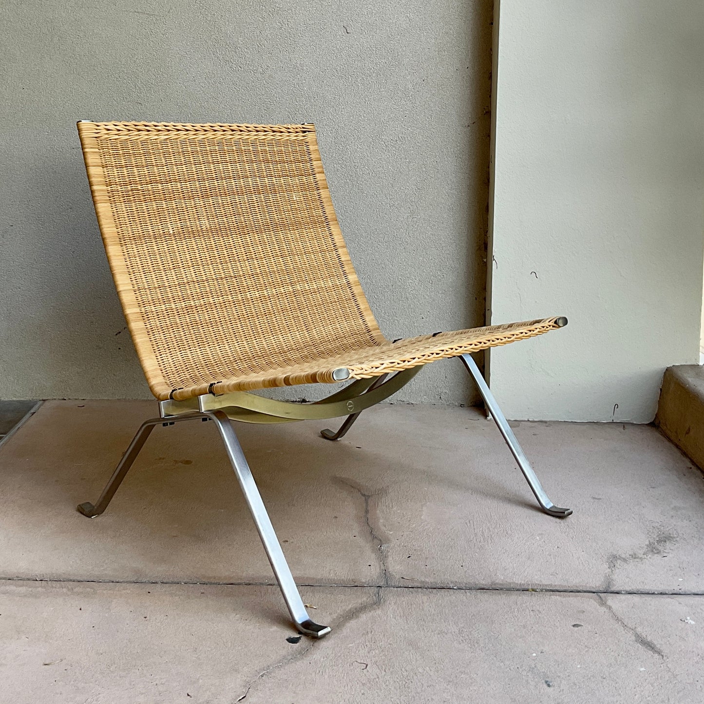 Woven chair with metal legs on a concrete floor against a wall.