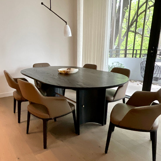 Grazia & Co Dining area with a round dark wooden table and beige chairs in a well-lit room.